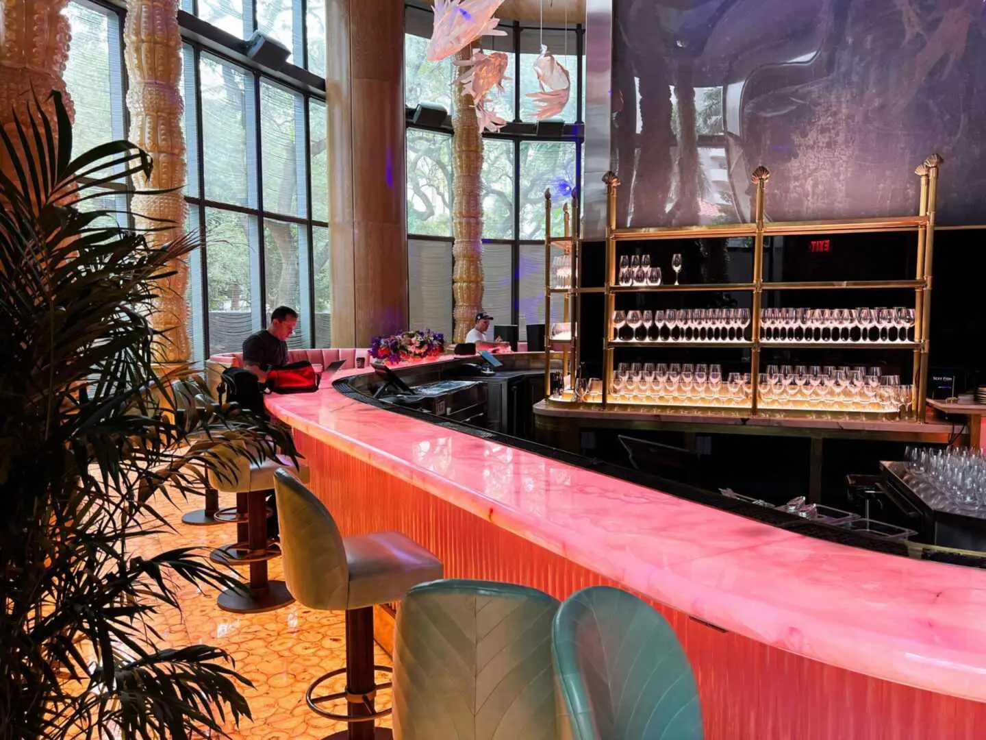 A bar with pink counter and chairs in front of a large window.